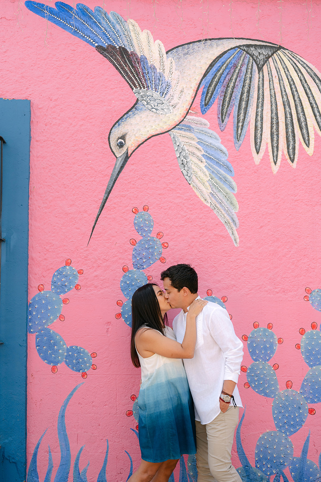 Ximena and Alexei kissing in front of a pink hummingbird mural